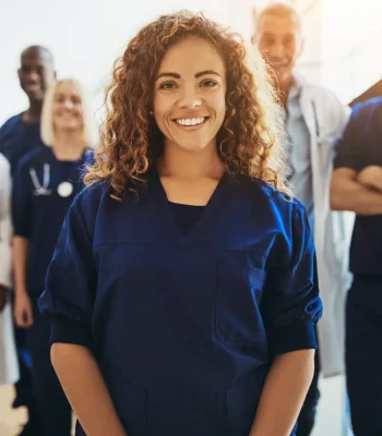 Smiling young female doctor standing in a hospital corridor with a diverse group of medical staff standing behind her