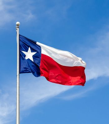 Texas State flag on the pole waving in the wing against blue sky and white clouds