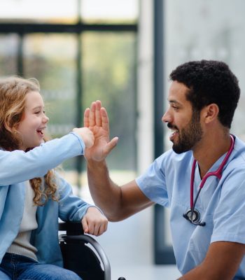 Young multiracial doctor having fun with little girl on a wheelchair.