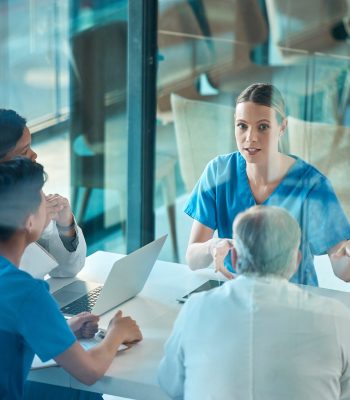 Medical team, doctors and meeting with a laptop for a discussion, planning or research at table. Men and women healthcare group talking about communication strategy, virus or surgery in a hospital.