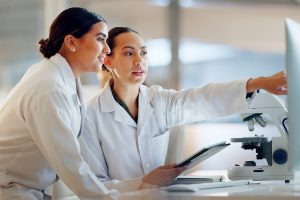 Scientist, women and teamwork on tablet and computer for laboratory advice, medical research and night planning. Students, science people or mentor on digital technology of test results or comparison.